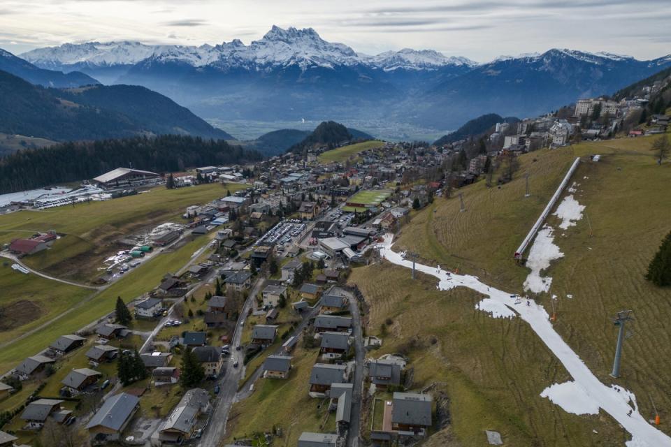 Skiers pass on a small layer of artificial snow amid warmer-than-usual winter temperatures in the Alps in Leysin, Switzerland on 4th January (REUTERS)