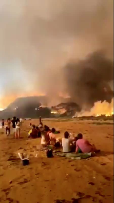 People watch as vegetation burns during bushfires near the coast of Rosedale