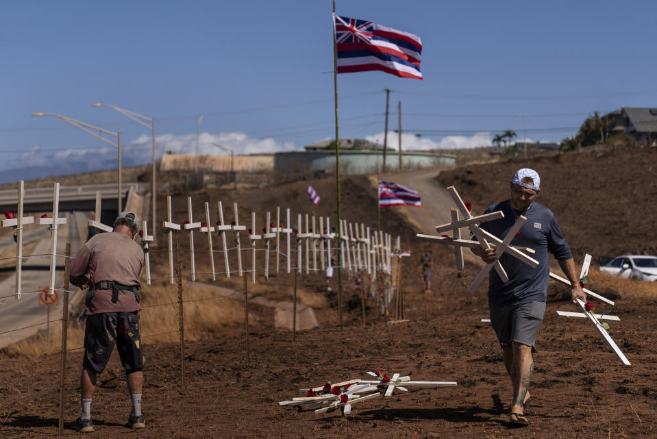 FILE - Ethan Meyers, right, carries crosses to put up to honor the victims killed in a wildfire in Lahaina, Hawaii, Aug. 22, 2023. The number of people still missing following wildfires that destroyed the historic community of Lahaina a month ago has dropped, Hawaii Gov. Josh Green said Friday, Sept. 8, 2023, while the number of confirmed deaths has remained at 115. (AP Photo/Jae C. Hong, File)