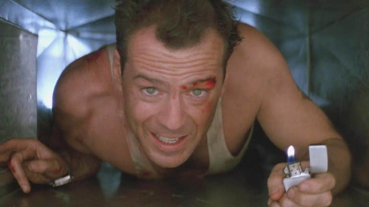 Bruce Willis as John McClane in Die Hard, crawling through a vent with a bloody face and a lighter in his hand.