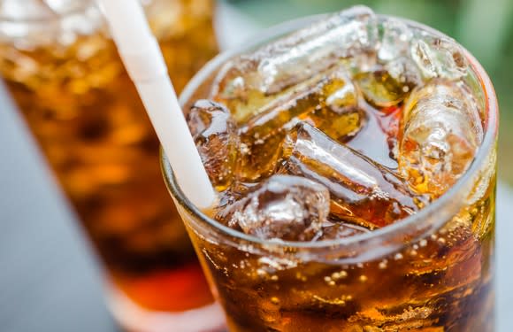 A glass of soda with ice and a straw.