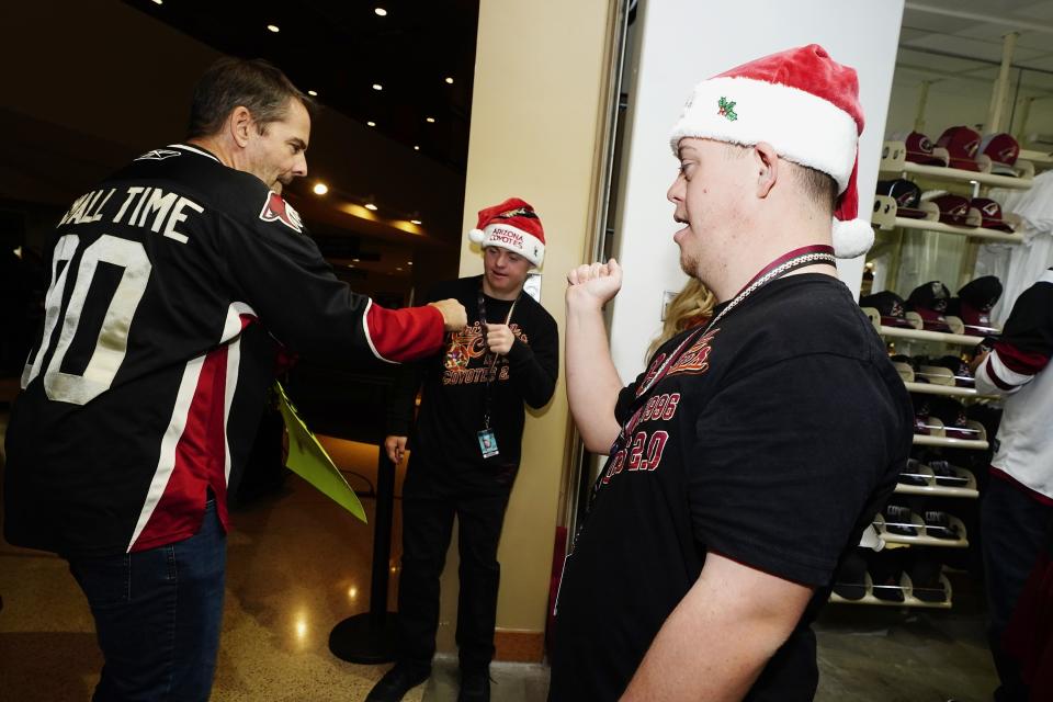 Angels for Higher representatives Matthew Adams, right, and Chase Baird, middle, greet an Arizona Coyotes fan at the entrance to the Coyotes' team shop prior to an NHL hockey game Dec. 3, 2021, in Glendale, Ariz. The job is a perfect fit for Matthew and Chase, two gregarious teens with Down syndrome. It's great for the Coyotes, too, an opportunity to expand the franchise's community outreach and inclusion programs. And, judging by the smiles and enthusiastic reactions to Matthew and Chase, it's also a big hit with Coyotes fans.(AP Photo/Ross D. Franklin)
