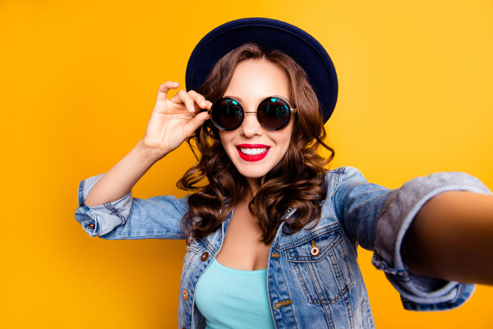 A young woman in a hat and sunglasses takes a selfie.