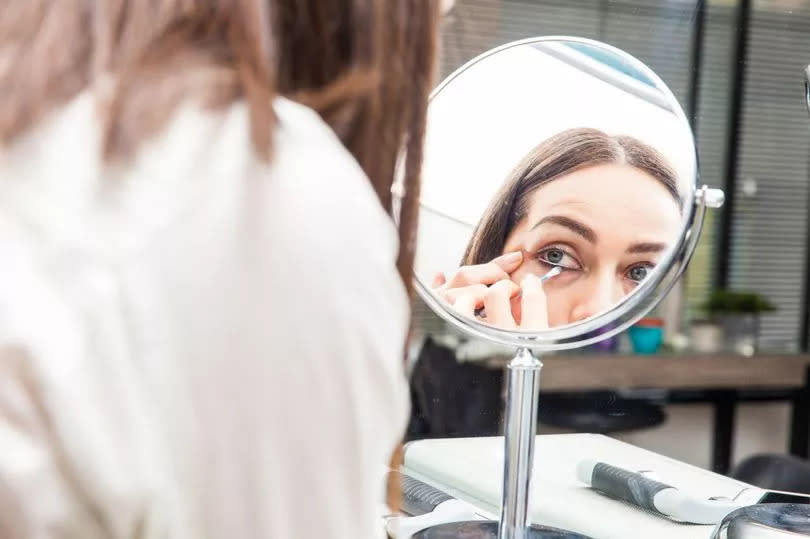 White woman removing makeup in front of mirror