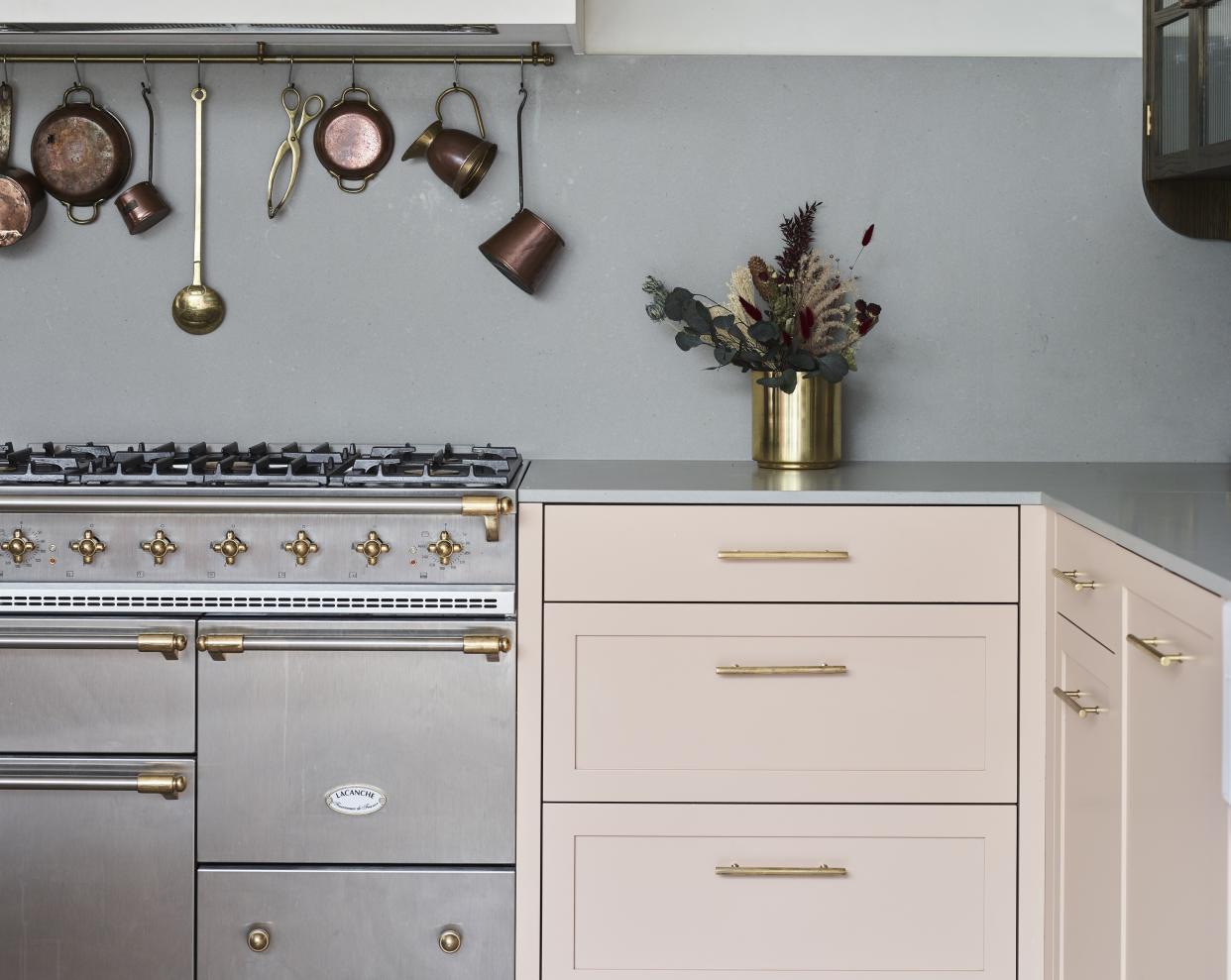  A kitchen with pastel pink cabinets and pans hanging up 