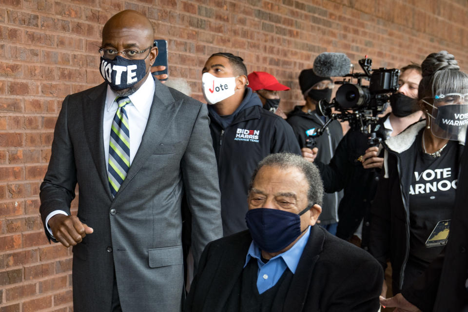 Warnock, wearing a mask that reads Vote, is accompanied by former Atlanta mayor and U.S. congressman Andrew Young as he casts his vote in the 2021 runoff election.