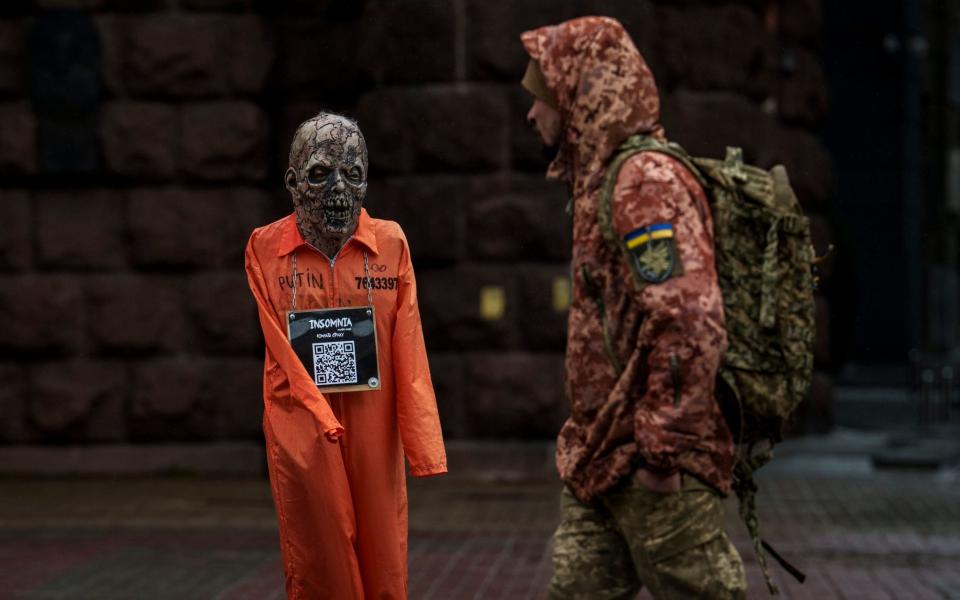 A Ukrainian serviceman walks by an effigy of Russian President Vladimir Putin dressed in a prisoner outfit during a rainfall in Kyiv