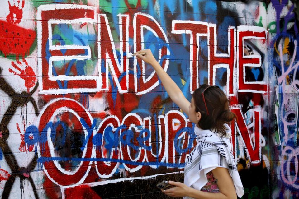 A student paints over graffiti to a pro-Palestinian mural on the side of Mead Hall on the Pitzer College campus.