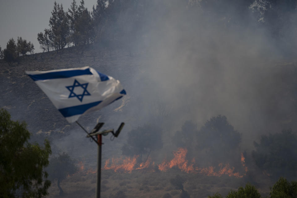 An Israeli flag flutters next to a fire burning in an area near the border with Lebanon, northern Israel in Safed, Wednesday, June 12, 2024. Scores of rockets were fired from Lebanon toward northern Israel on Wednesday morning, hours after Israeli airstrikes killed four officials from the militant Hezbollah group including a senior military commander. (AP Photo/Leo Correa, File)