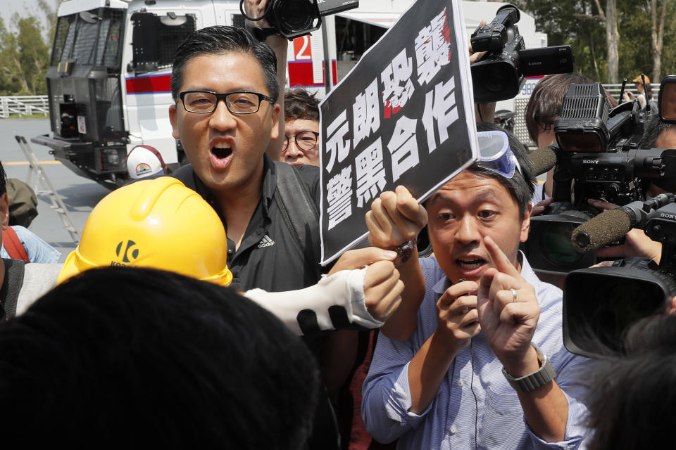 Pro-democracy lawmakers Lam Cheuk-ting, left, and Ted Hui, right, argue with pro-Beijing lawmaker Junius Ho during a demonstration of an anti-riot vehicle equipped with water cannon at the Police Tactical Unit Headquarters in Hong Kong on Aug. 12, 2019. Hong Kong police on Wednesday morning, Aug. 26, 2020 arrested 16 people on charges related to anti-government protests last year, including two opposition lawmakers Hui and Lam. The placard reads "Yuen Long terrorist attack, collusion between police and triads." (AP Photo/Kin Cheung)