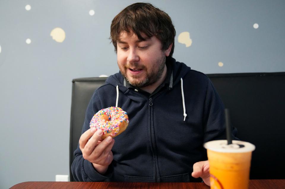 IndyStar reporter Rory Appleton sizes up a frosted yeast doughnut Thursday, March 23, 2023, at PANA Donuts on the south side of Indianapolis. Appleton has crowned PANA Donuts as Indy's best doughnuts, citing their soft, pillowy texture. 