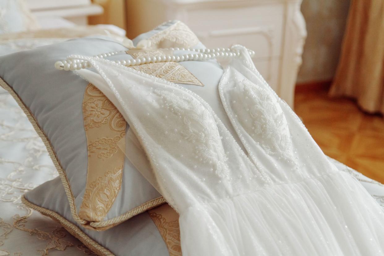 Wedding dress with hanger laying on the bed.