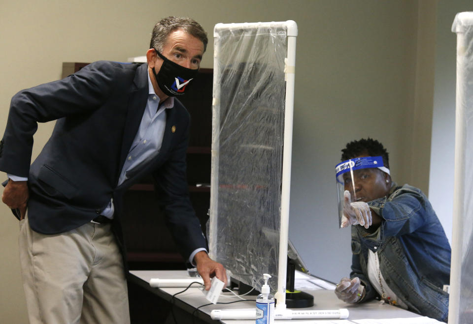 Virginia Gov. Ralph Northam, left, is shown by a poll worker which way to go as he votes early at the Richmond general registrar's office in Richmond, Va., Friday, Sept. 18, 2020, on the first day of Virginia's 45-day early voting period. (Bob Brown/Richmond Times-Dispatch via AP)