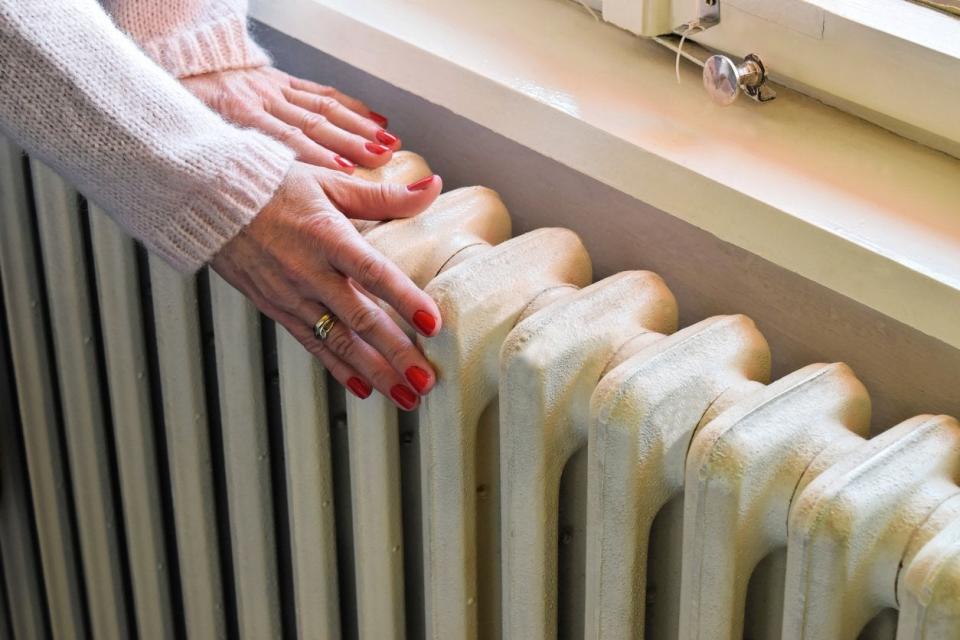 Woman wearing a sweater touches a radiator on her wall. 