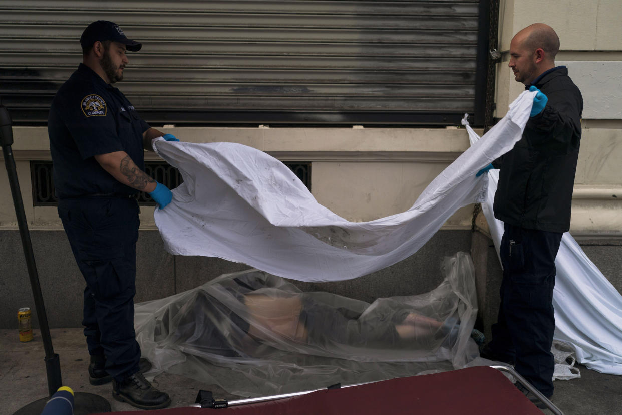 Forensic assistant Laurentiu Bigu, left, and investigator Ryan Parraz from the Los Angeles County coroner's office cover the body of a homeless man found dead on a sidewalk in Los Angeles, Monday, April 18, 2022. The 60-year-old man died from the effects of methamphetamine, according to his autopsy report. Nearly 2,000 homeless people died in the city from April 2020 to March 2021, a 56% increase from the previous year, according to a report released by the Los Angeles County Department of Public Health. Overdose was the leading cause of death, killing more than 700. (AP Photo/Jae C. Hong)