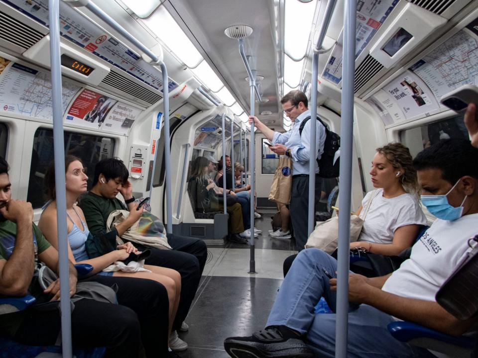 Fahrgäste sitzen in einem Londoner U-Bahn-Wagen, einer hält sich an der grauen Stange der Jubilee Line fest.