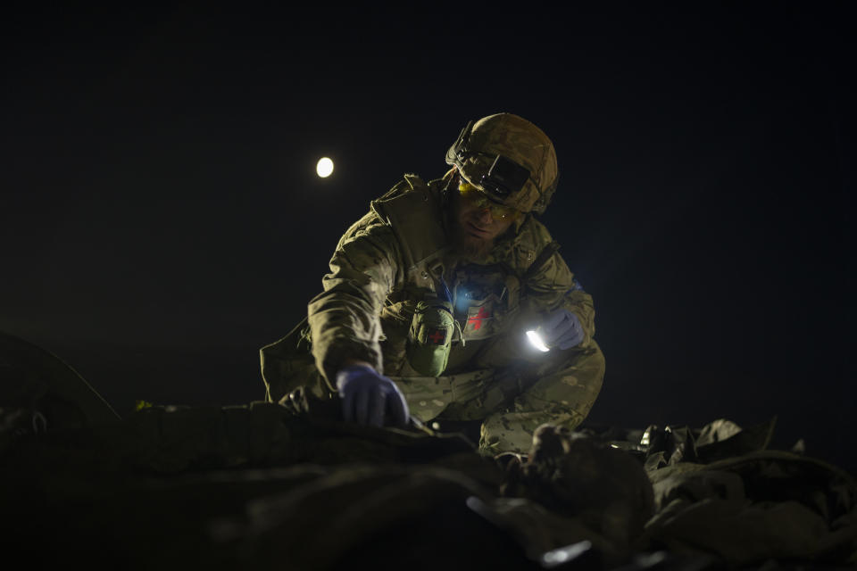 Oleksii Yukov examines the body of a Russian soldier he collected on the frontline in the Sloviansk region, Ukraine, Tuesday, Oct. 24, 2023. The 38-year-old martial arts instructor leads a team of volunteer body collectors in Ukraine. (AP Photo/Bram Janssen)