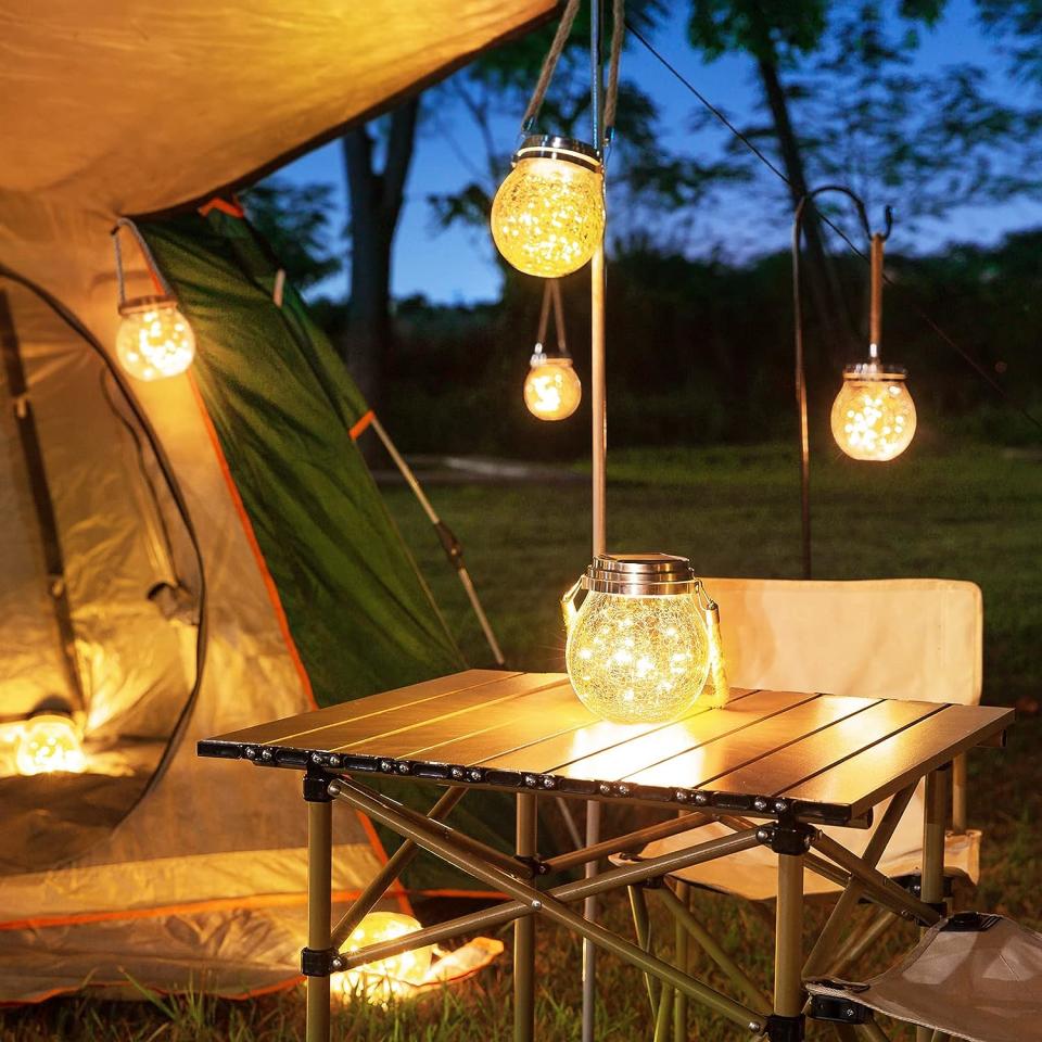 Camp site with a tent and table lit by warm string light lanterns