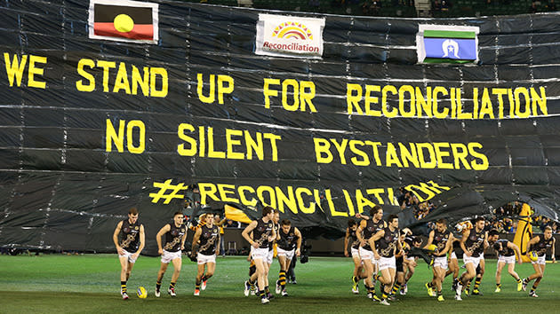 Richmond players run through a banner paying tribute to Adam Goodes.