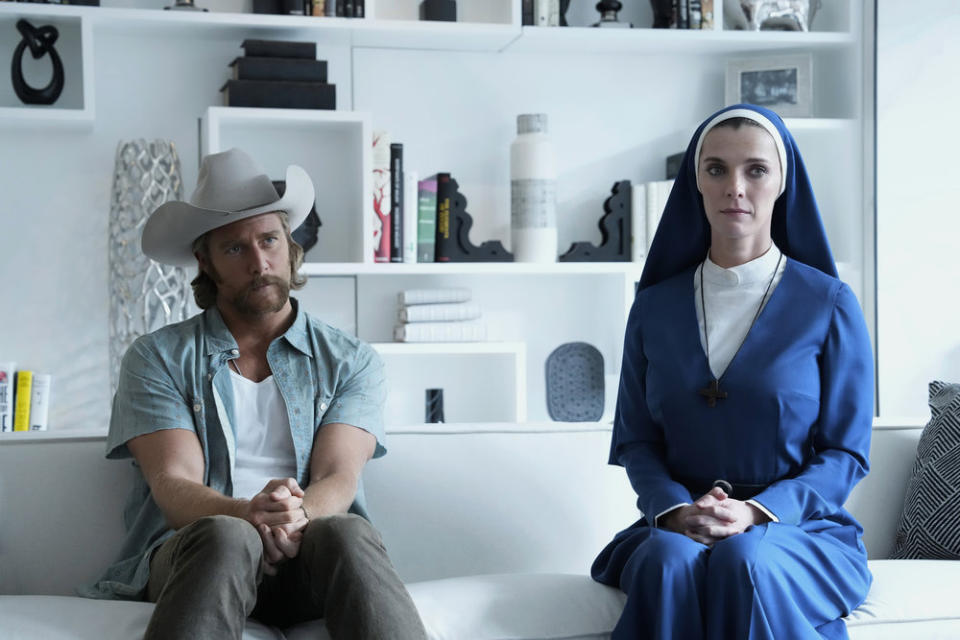 A nun and a cowboy sit a foot apart from each other on a white coach in a pristine white office; still from "Mrs. Davis"