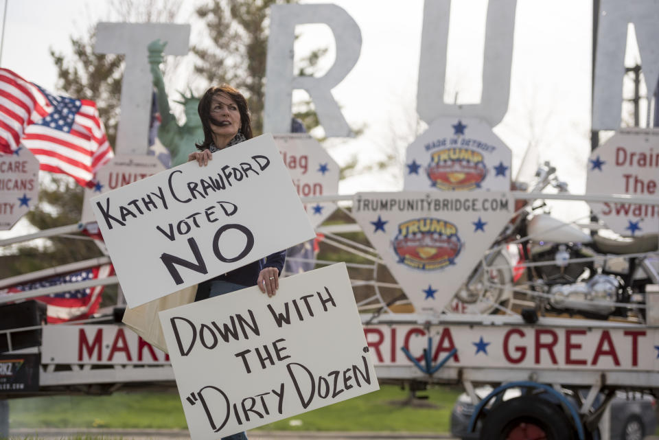 FILE - Marian Sheridan, of West Bloomfield, holds two different signs while participating in the protest at the post office on the failure to reduce Michigan's tax rate Tuesday, April 18, 2017, in Novi, Mich. Michigan Attorney General Dana Nessel has charged 16 Republicans Tuesday, July 18, 2023, with multiple felonies after they are alleged to have submitted false certificates stating they were the state’s presidential electors despite Joe Biden’s 154,000-vote victory in 2020. The group includes Republican National Committeewoman Kathy Berden, Meshawn Maddock, former co-chair of the Michigan Republican Party, and Sheridan. (David Guralnick/Detroit News via AP)