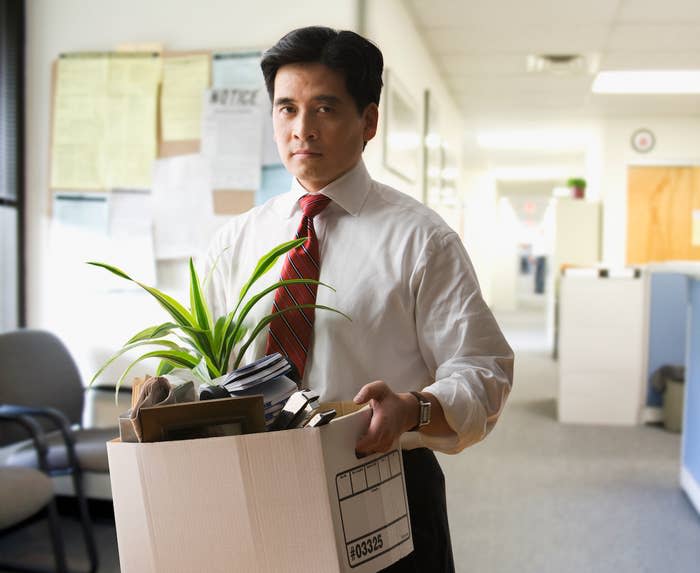 Man wearing a shirt and tie carries a box of his belongings out of an office