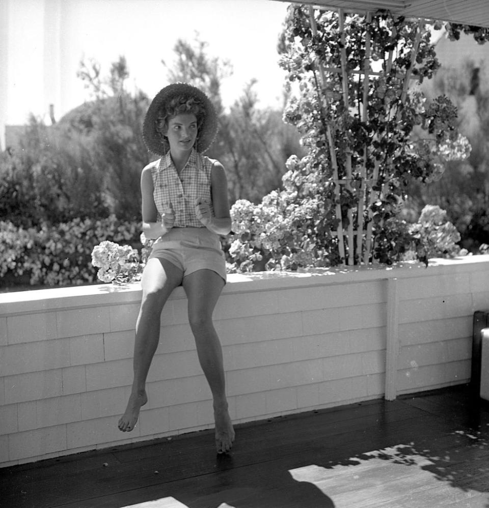 <p>Jackie sports a gingham button-down blouse and a straw hat—ever the picture of ease and graciousness—while vacationing at the Kennedy compound in Massachusetts.<br></p>