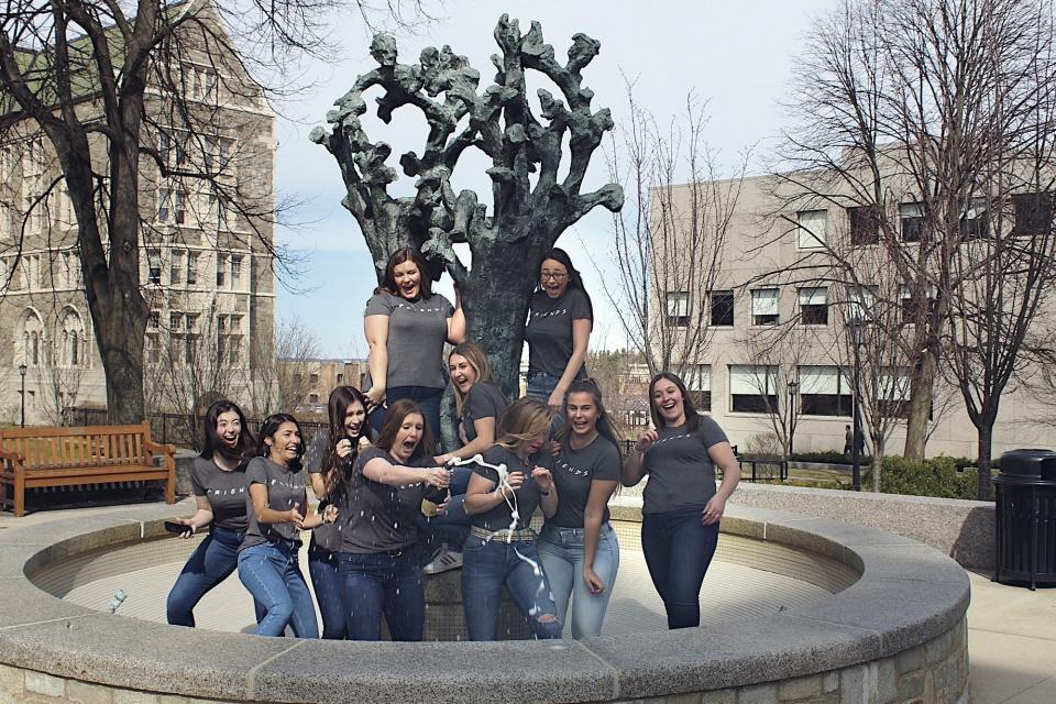 In this March 14, 2020 photo provided by Jaimie Kirkpatrick, Boston College seniors pop champagne beside the Tree of Life sculpture on the school's campus in Boston. It is uncertain if the campus will reopen in time for graduation. (Jaimie Kirkpatrick via AP)