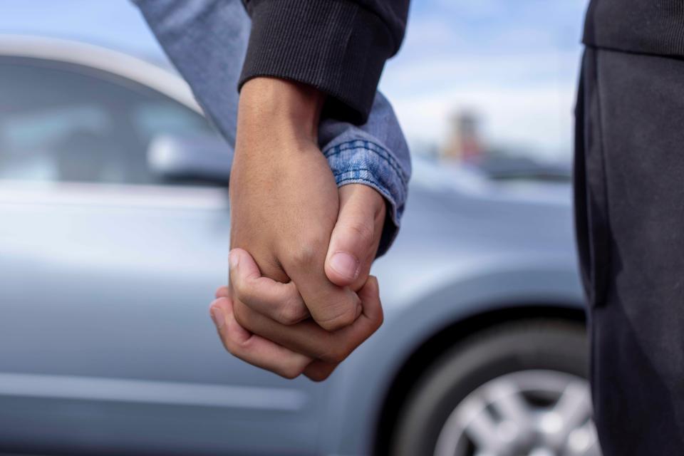 A couple holding hands in front of a car.