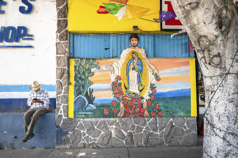 In this photo by Oscar Rodriguez Zapata, a man checks his phone near a Virgin of Guadalupe mural in Los Angeles in July 2020. Across the city, images of the Virgin are believed to thwart vandalism and act as “protector(s) of small immigrant-owned businesses,” according to journalist Sam Quinones’ 2016 book of photographs of murals of the saint, “The Virgin of the American Dream.” (Oscar Rodriguez Zapata via AP)