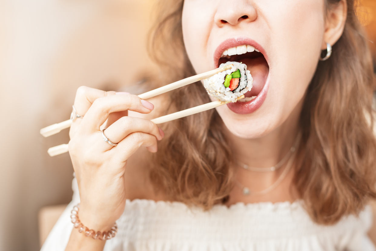 Woman Putting a Piece of Sushi, With Chopsticks, in Her Mouth