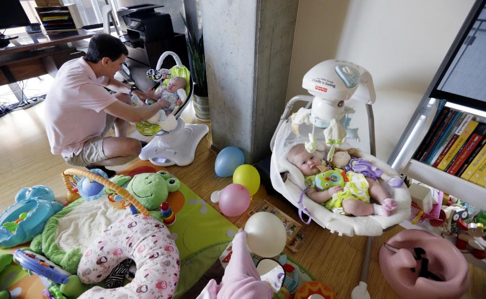 In this Tuesday, Aug. 20, 2013 photo, Trey Powell settles his six-month-old daughter Kylan down for a nap as her twin sister, Ashton, lies nearby in their home in Seattle. (AP Photo/Elaine Thompson)