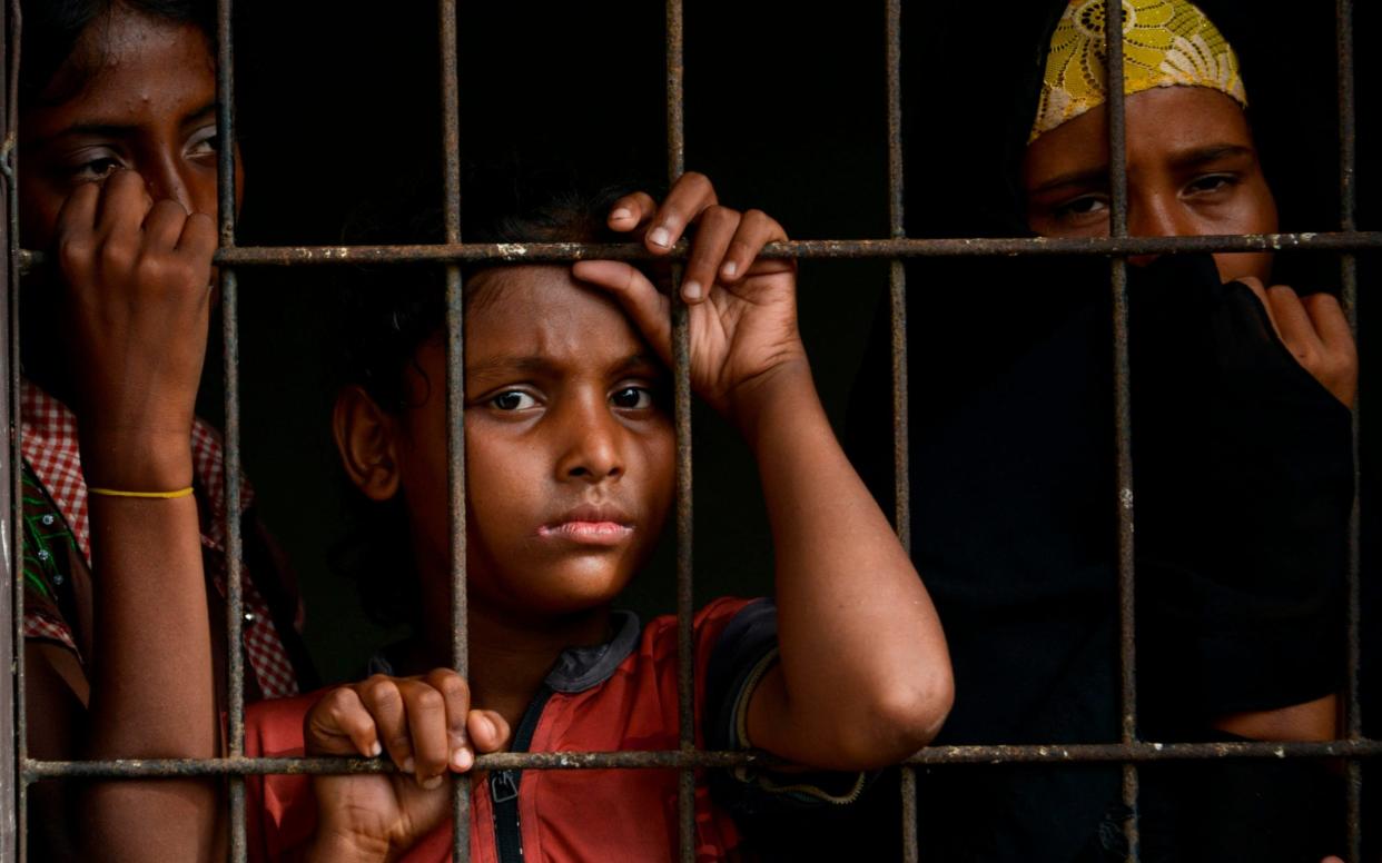 Rohingya people from Myanmar look through a fence at the immigration detention centre in Lhokseumawe, in Indonesia's North Aceh Regency - CHAIDEER MAHYUDDIN/AFP