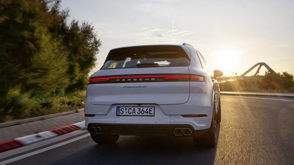 2024 porsche cayenne turbo e hybrid from the rear driving toward a bridge at dusk