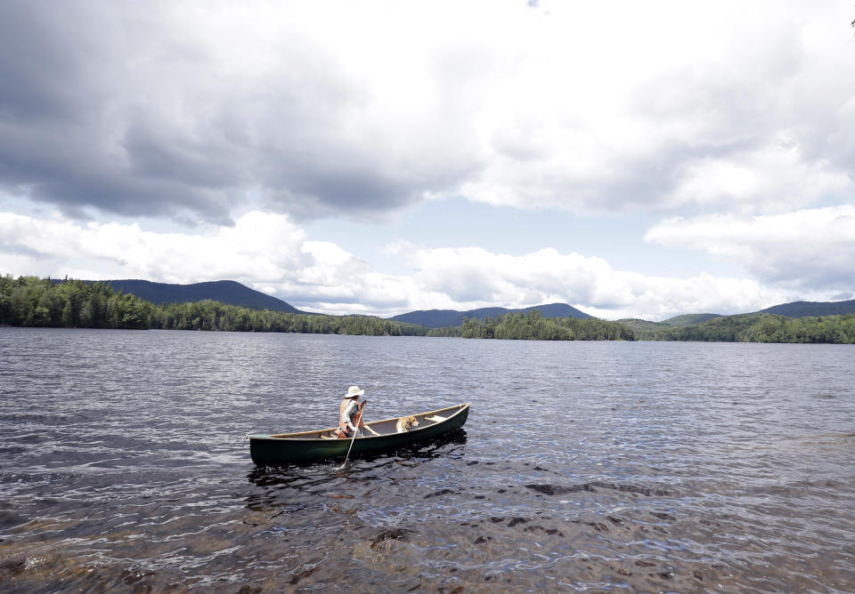 In this Tuesday, July 30, 2013 photo, Cynthia Taylor, of Watertown, Mass., canoes along the shoreline of Camp Santanoni on Newcomb Lake with her dog Arlo, in Newcomb, N.Y. Camp Santanoni is an Adirondack Mountain great camp that is being restored. (AP Photo/Mike Groll)