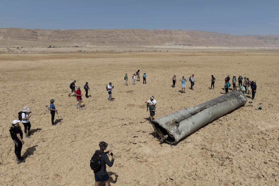 People gather around a component from an intercepted ballistic missile that fell near the Dead Sea in Israel, Saturday, April 20, 2024. Open fighting between Israel and Iran began April 1 with the suspected Israeli killing of Iranian generals at an Iranian diplomatic compound in Syria. That prompted Iran's retaliatory barrage last weekend of more than 300 missiles and drones that the U.S., Israel and regional and international partners helped bat down without significant damage in Israel. And then came Friday's strikes that hit near military and nuclear targets in Iran. (AP Photo/Itamar Grinberg)