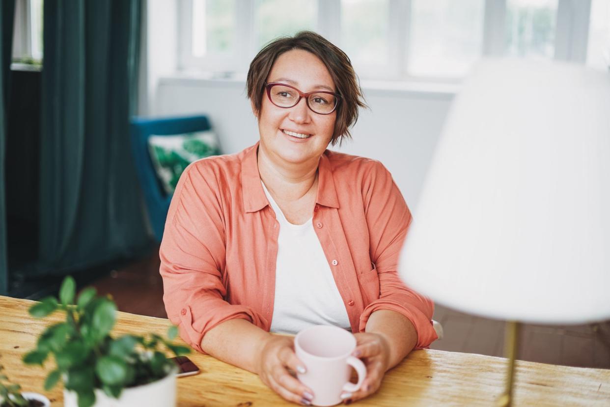 Adult charming brunette woman in glasses plus size body positive with cup of tea at home