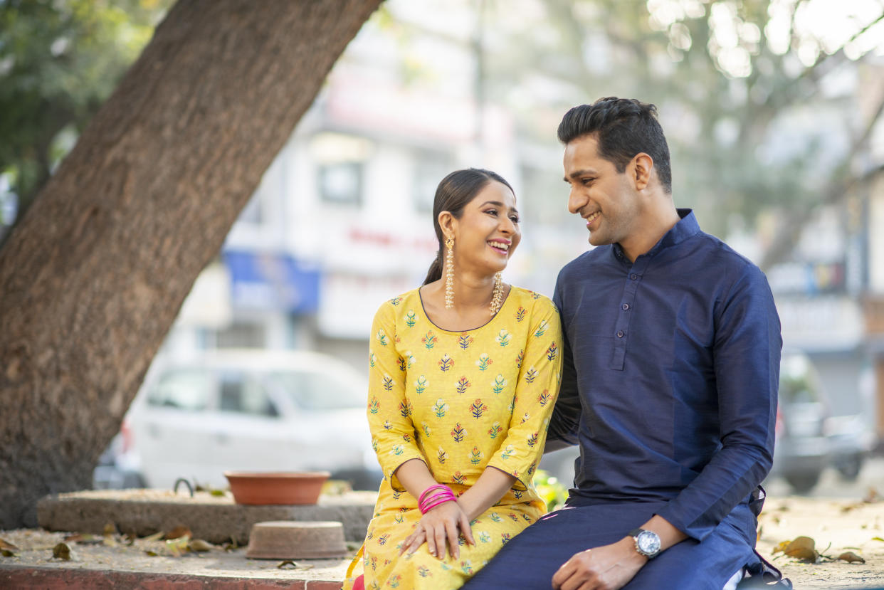 An Indian couple sits side by side while looking at each other lovingly. They are incredibly happy.