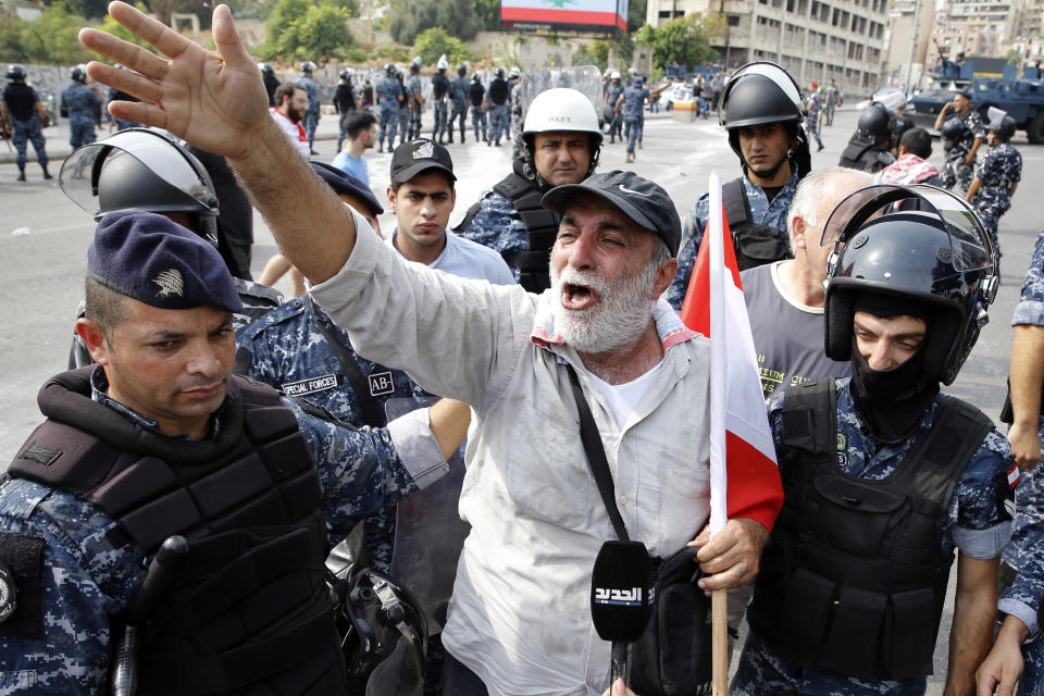 An anti-government protester, center, weeps after riot police prepare to remove him and open the road in Beirut, Lebanon, Saturday, Oct. 26, 2019. The removal of the roadblocks on Saturday comes on the tenth day of protests in which protesters have called for civil disobedience until the government steps down. (AP Photo/Bilal Hussein)