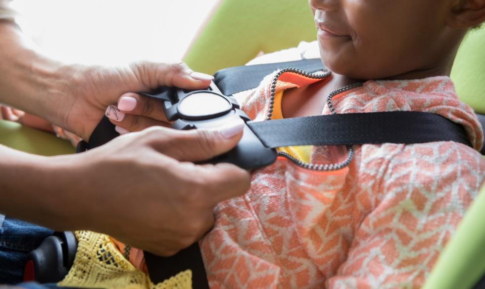 African American girl is strapped into a booster seat in a car