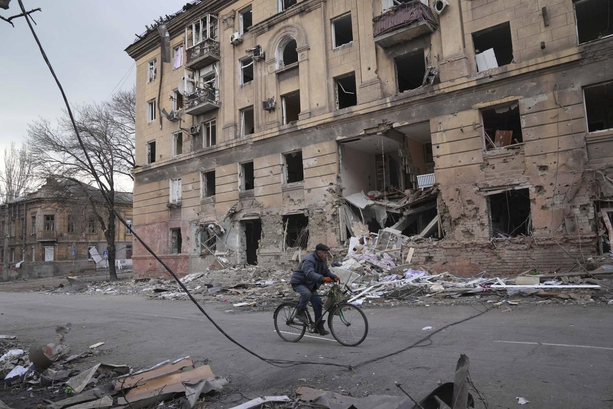 A man rides a bicycle in front of an apartment building damaged by shelling in Mariupol, Ukraine, Wednesday, March 9, 2022.