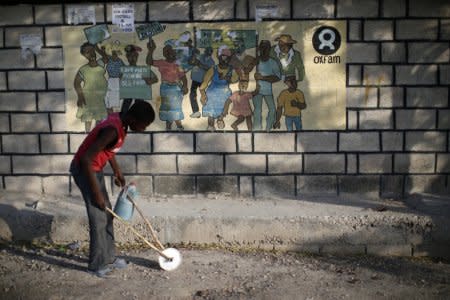 A boy playing with a homemade toy walks past an Oxfam sign in Corail, a camp for displaced people of the earthquake of 2010, on the outskirts of Port-au-Prince, Haiti, February 17, 2018. REUTERS/Andres Martinez Casares