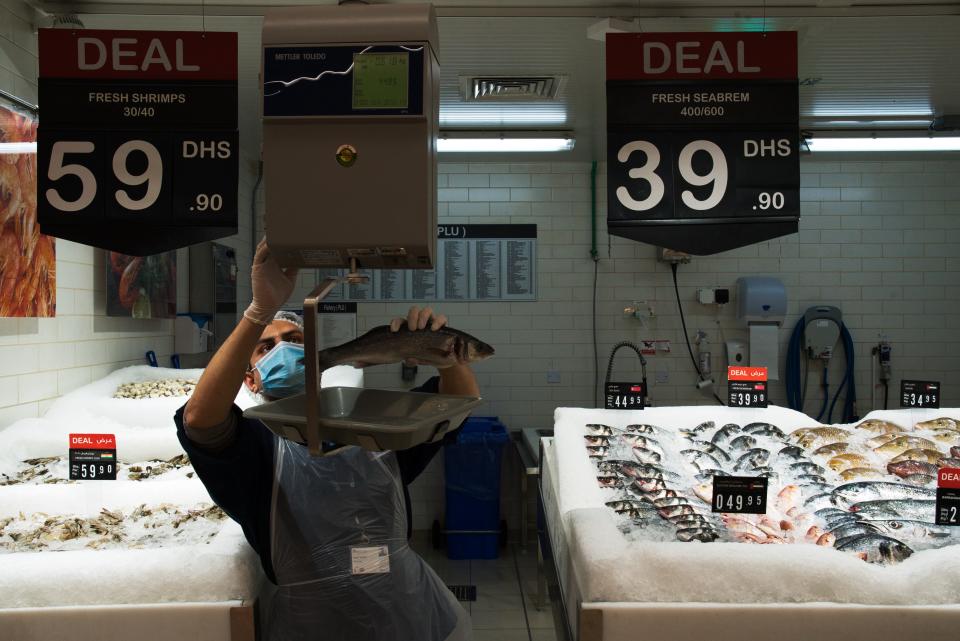 In this Sunday, April 19, 2020 photo, fishmonger Ramu Subedi of Nepal weighs a fish at a Carrefour supermarket while wearing a face mask amid the coronavirus pandemic in Dubai, United Arab Emirates. Frontline workers across Arab Gulf countries are uniquely almost entirely foreigners. They risk exposure to the virus, ensuring patients are cared for, streets are sanitized, packages are delivered and grocery stores are stocked. The global pandemic has drawn attention to just how vital foreigners are to the Arab Gulf countries where they work. (AP Photo/Jon Gambrell)