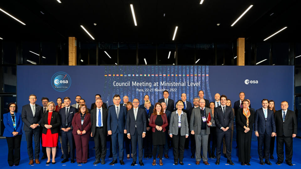 several dozen well-dressed people stand in front of a blue background during a conference