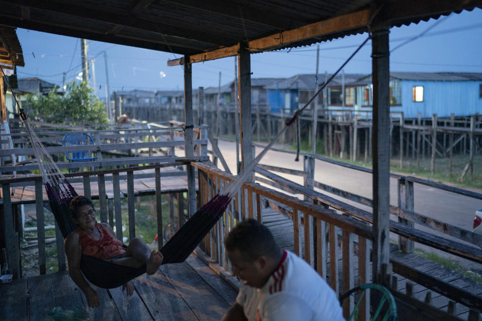 In this Nov. 27, 2019 photo, Antonia Pereira swings on her hammock as she talks with a friend on her stilt house at the Vila Nova neighborhood in Itaituba, Para state, Brazil. She says life was better in the 1980s when people came to the gold mines in the region. Now she survives selling hammocks and cooking street barbecues. Sometimes she can fish from her porch during the season that the Tapajos river floods. "I wish there were more jobs for the young people," she says. (AP Photo/Leo Correa)