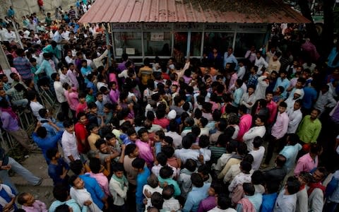 Indian migrant workers wait outside the government transport yard as they seek to buy bus tickets out of Kashmir - Credit: AP