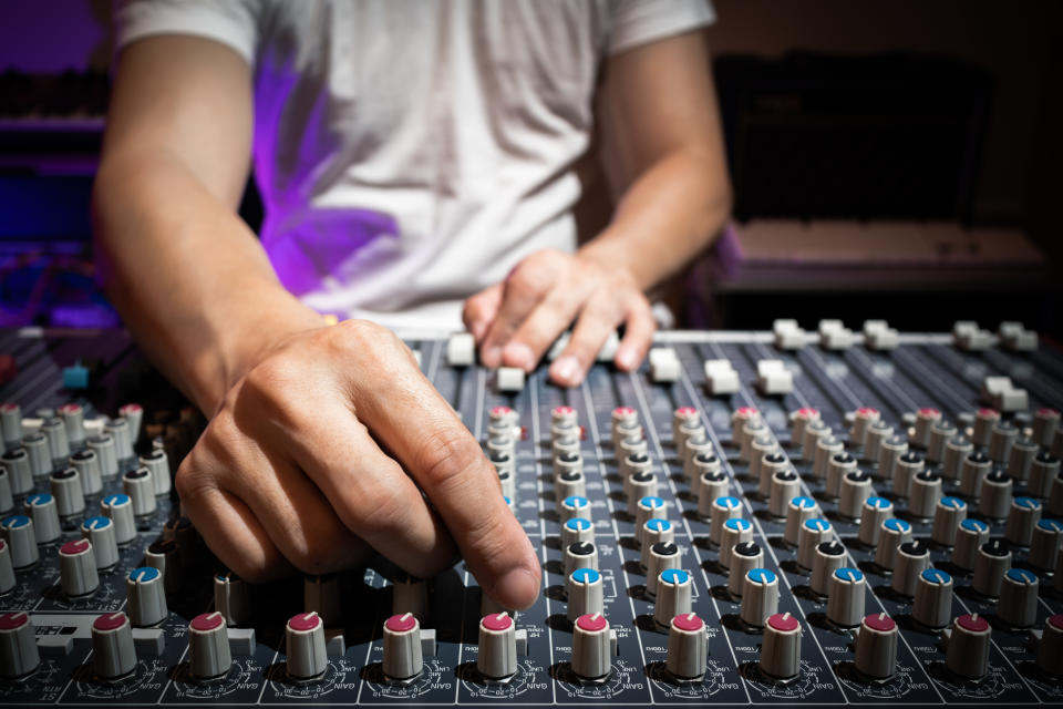 A person adjusts audio levels on a sound mixing board