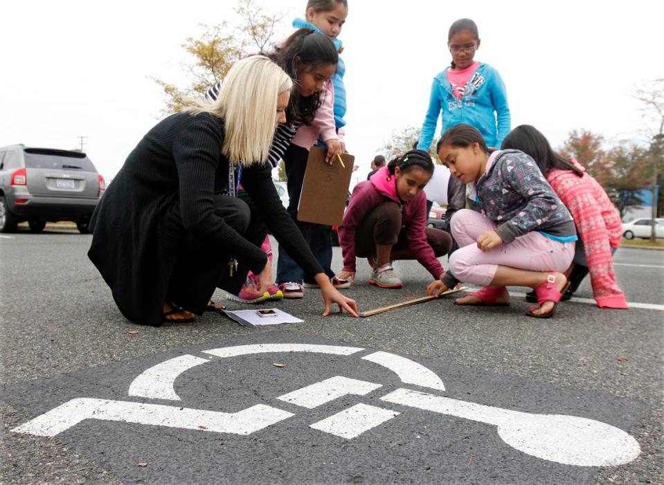To see if a school parking spot was up to standards for width, Bethesda Elementary reading specialist Emily Smith, left, guided a group of Bethesda 4th graders in how to measure the actual width of the parking space Tuesday Oct. 29, 2013.