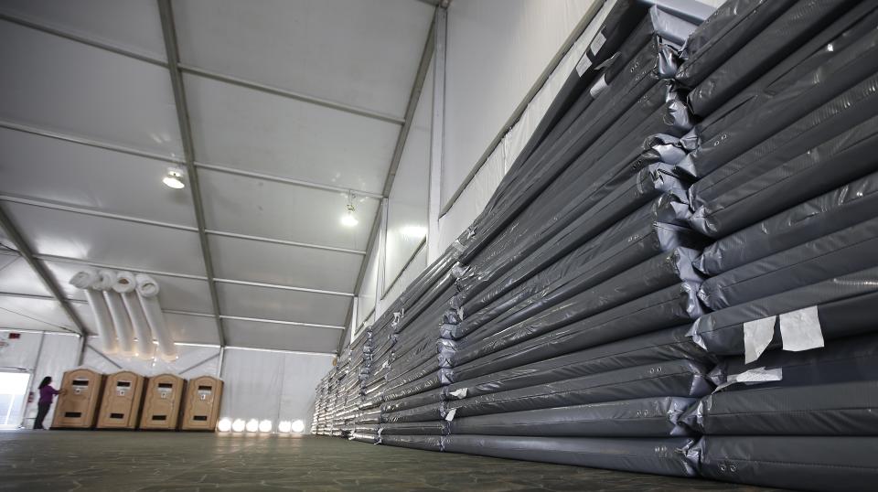 Temporary mattress pads are stacked up along a tent wall with restroom facilities in the background, as the U.S. Border Patrol unveiled a new 500-person tent facility during a media tour Friday, June 28, 2019, in Yuma, Ariz. The facility will be used to process detained immigrant children and families who cross the U.S. border. The Border Patrol says it will start placing families there on Friday night. (AP Photo/Ross D. Franklin)