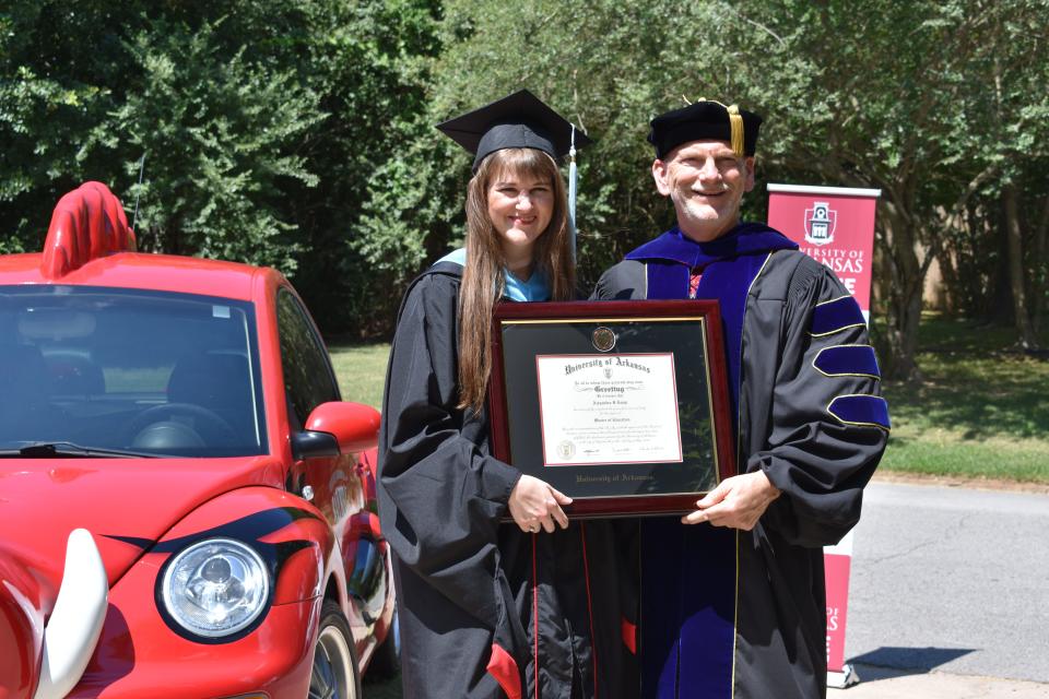 Alexandra Lemp, left, of Fort Smith receives a framed diploma Friday for her master's degree in educational leadership from Ed Bengtson, head of the Department of Curriculum and Instruction at the University of Arkansas.